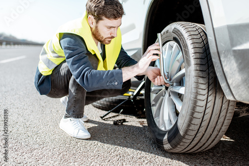 Man in vest unscrewing the broken wheel on the roadside photo