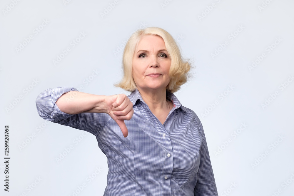 Displeased blonde senior woman showing thumb down. Displeased blonde senior woman showing thumb down.