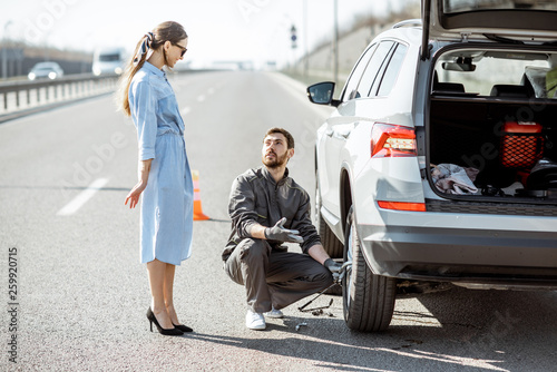 Photography Road assistance worker helping young woman to change a car wheel on the highway