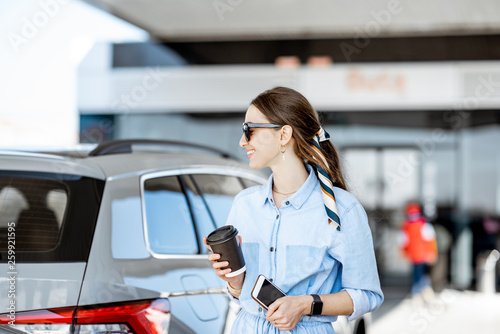 Young woman having a coffee break standing near the car on the gas station photo