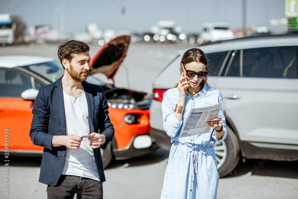 Φωτογραφία Man and woman arguing, standing together on the road with their cars on the back