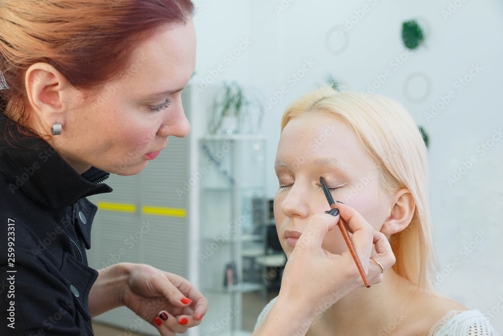 Process of making makeup. Make-up artist working with brush on model face. Portrait of young blonde woman in beauty saloon interior. Applying tone to skin. Process of making makeup. Make-up artist working with brush on model face. Portrait of young blonde woman in beauty saloon interior. Applying tone to skin.