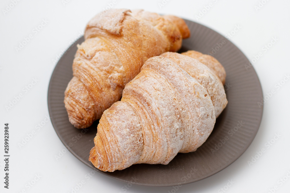 breakfast croissants sprinkled with powdered sugar on a gray plate. white background breakfast croissants sprinkled with powdered sugar on a gray plate. white background