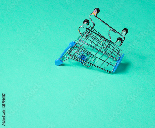 Minimalist shopping concept. Empty inverted miniature shopping trolley on blue background
