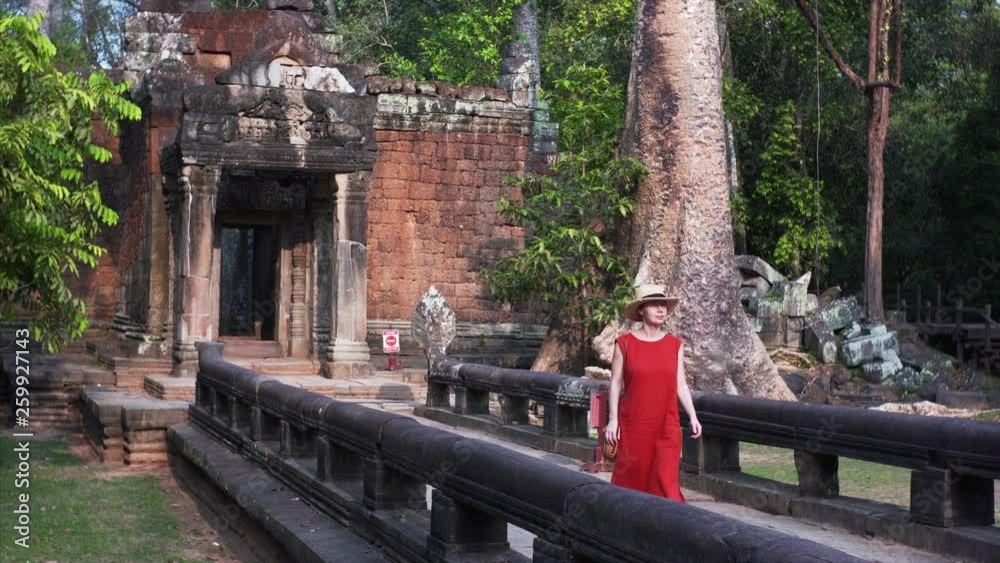 Attractive young woman walking through the temple morning. Woman in the red dress strolling through the temple in Cambodia, Angkor, Ta Prohm Temple. Attractive young woman walking through the temple morning. Woman in the red dress strolling through the temple in Cambodia, Angkor, Ta Prohm Temple.