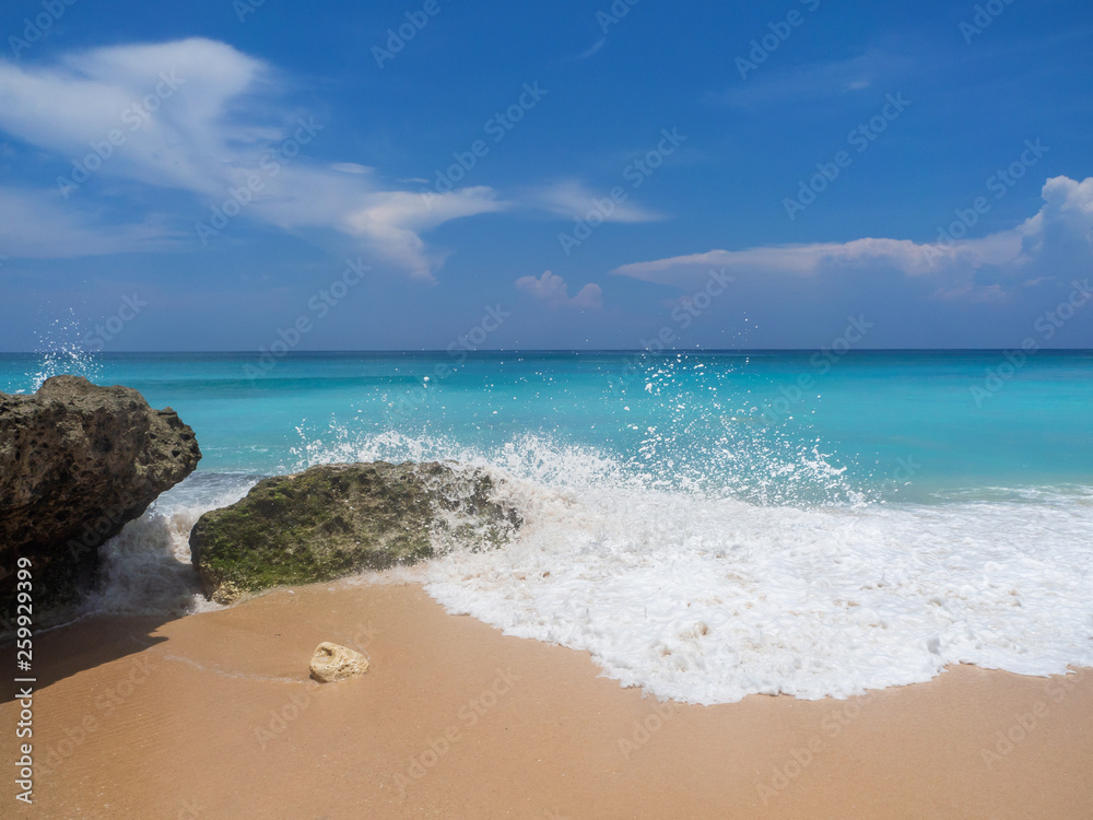 Turquoise waves crash against stones with splashes. Bali.