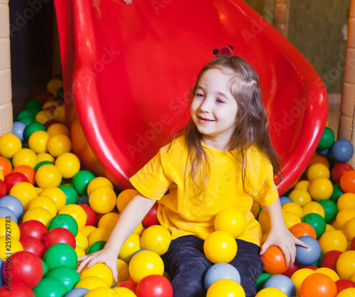 Happy little girl playing and having fun at kindergarten with colorful balls in play center photo