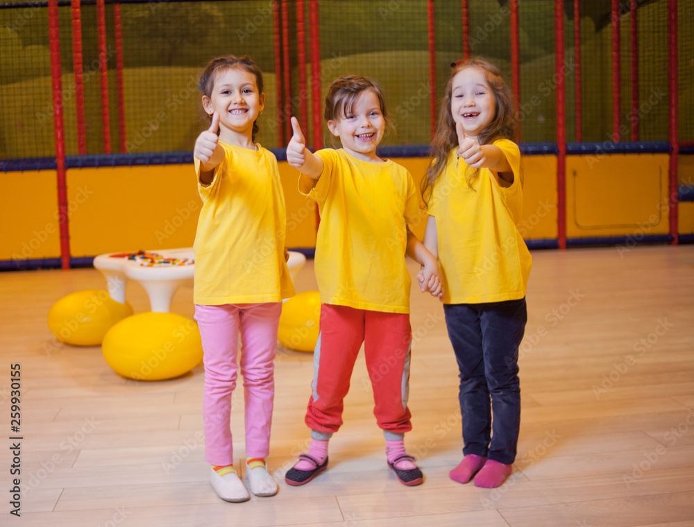 Obraz premium Three funny girls show thumb up in children's entertainment center