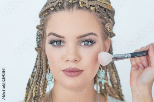 Professional makeup artist working with beautiful young woman. bright blonde model with african pigtails on a white background