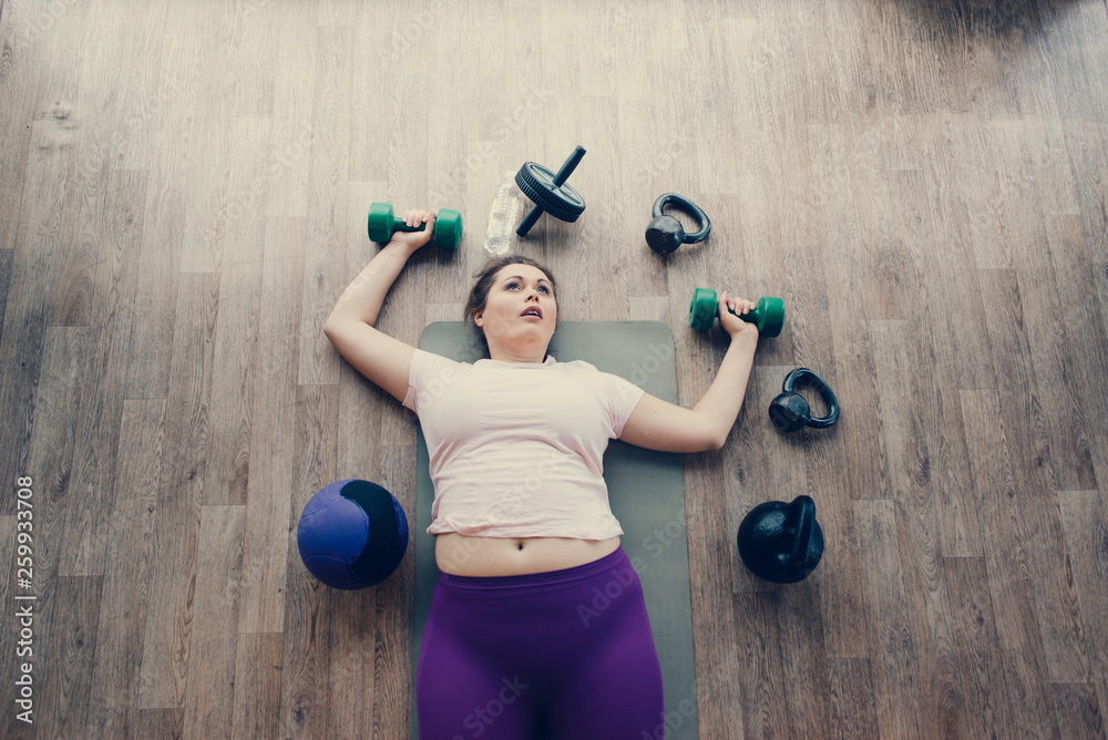 Fat woman lying exhausted on floor in fitness club Fat woman lying exhausted on floor in fitness club