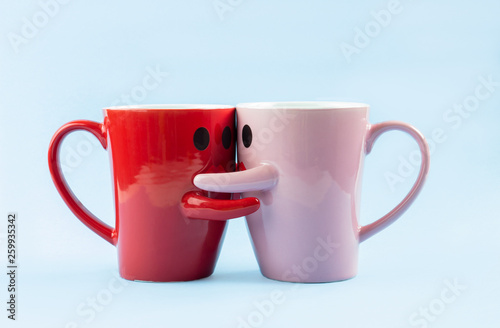 Friday's happy word. Two cups of coffee on a blue background with a smile facing the mug, hugging each other. The concept of love and relationships. Creative colorful greeting card