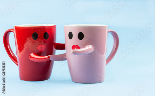 Friday's happy word. Two cups of coffee on a blue background with a smile facing the mug, hugging each other. The concept of love and relationships. Creative colorful greeting card
