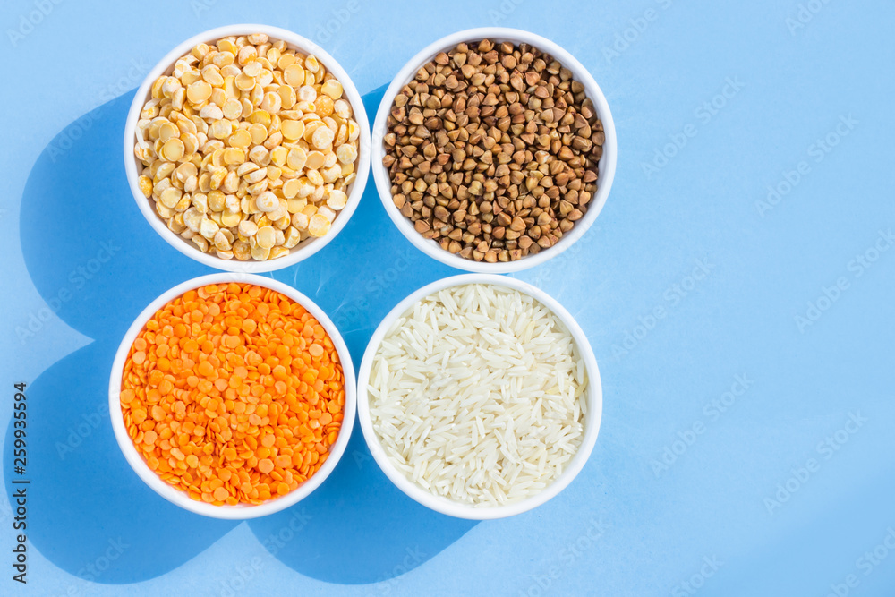 Assorted different cereals on a blue background. Buckwheat, lentils, rice, peas in plates top view, copy space Assorted different cereals on a blue background. Buckwheat, lentils, rice, peas in plates top view, copy space