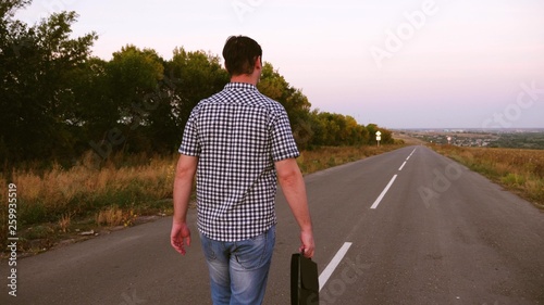 man walks along an asphalt road with black briefcase in his hand © zoteva87