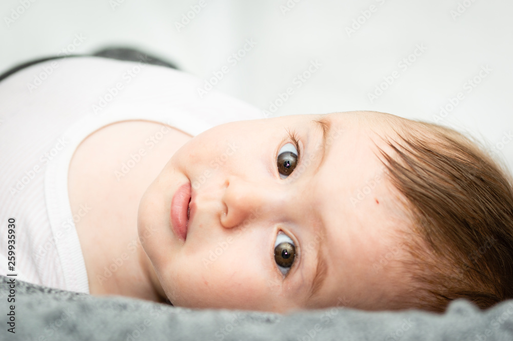 adorable blond baby lying on back on white bed