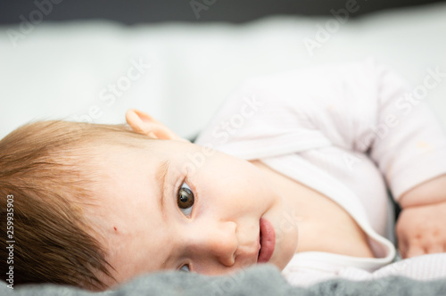 adorable blond baby lying on back on white bed