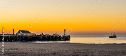 the harbor pier at the beach of blankenberge, Belgium, a boat sailing in the sea, beautiful sunset and colorful sky photo