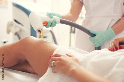 Fotografia Medical worker using laser tool for removing stretches on the leg of client