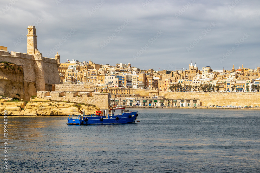 Mediterranean view with a tugboat, part of Fort St. Angelo in Birgu and Valletta with Quarry Wharf under a moody sky, at Grand Harbor, Malta
