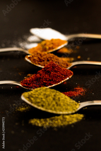 Kitchen concept: Variety of spices, silver spoons, black background, selective focus