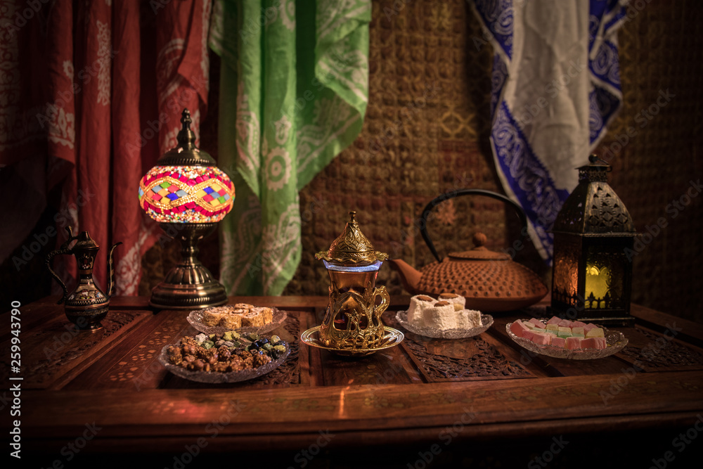 Arabian tea in glass with eastern snacks on vintage wooden surface. Eastern tea concept. Low light lounge interior with carpet. Empty space.