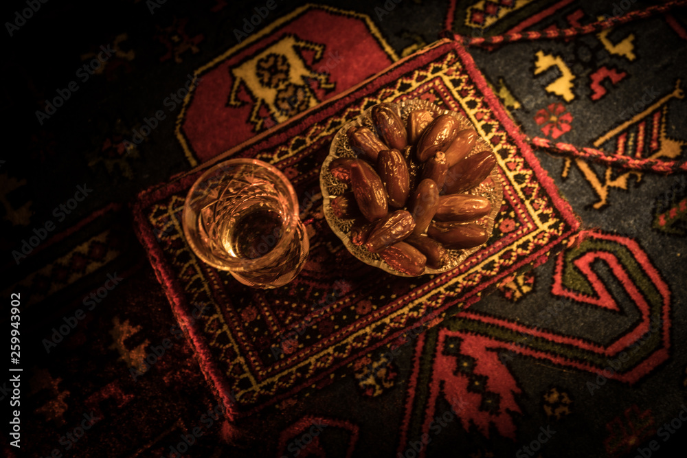 Water and dates. Iftar is the evening meal. View of decoration Ramadan Kareem holiday on carpet. Festive greeting card, invitation for Muslim holy month Ramadan Kareem. Dark background Water and dates. Iftar is the evening meal. View of decoration Ramadan Kareem holiday on carpet. Festive greeting card, invitation for Muslim holy month Ramadan Kareem. Dark background