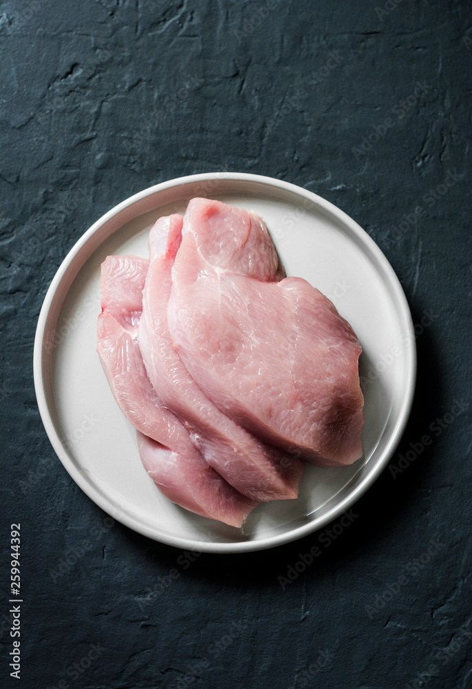 Raw turkey fillet chops on dark background, top view. Food ingredients