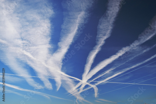 Many chemtrails or contrails  produced by airplanes flying on blue sky over the city