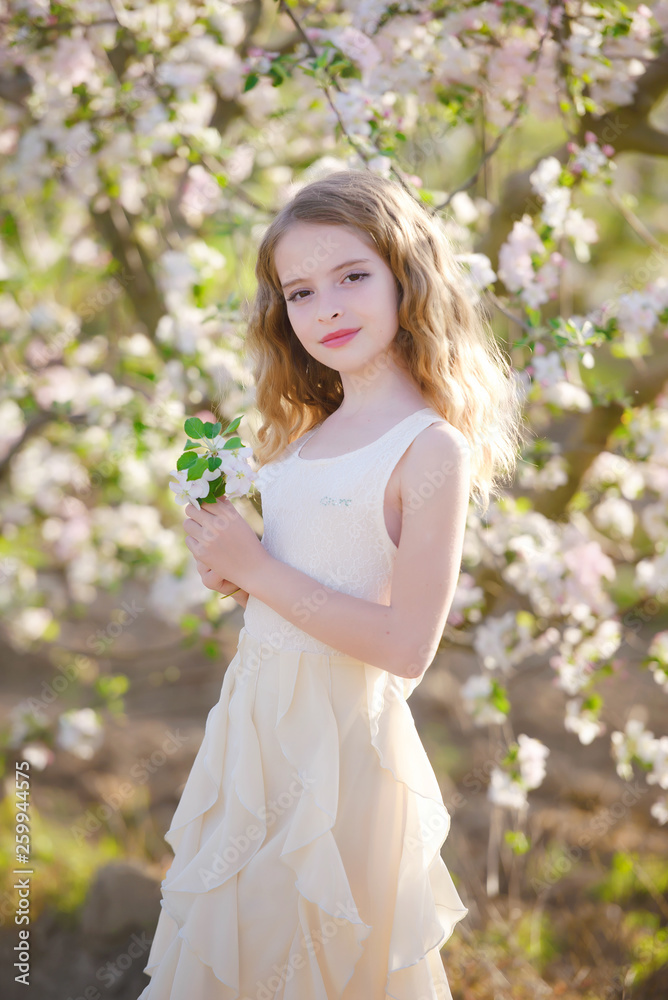 Gorgeous blonde girl standing near blossom tree and smiling. Girl near tree. Blonde girl outdoor smiling. Girl in garden. Young female in blossoming orchard. Spring concept. 