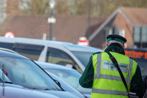 civil enforcement officer or traffic warden writes out parking ticket for vehicle in UK