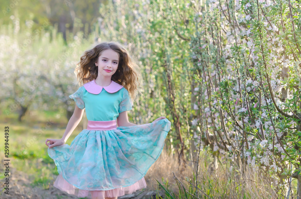 Gorgeous blonde girl standing near blossom tree and smiling. Girl near tree. Blonde girl outdoor smiling. Girl in garden. Young female in blossoming orchard. Spring concept. 