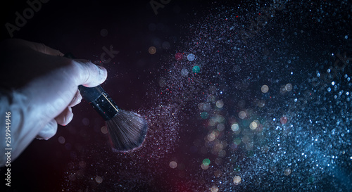Makeup brush in hand with cosmetic powder on dark background with light and smoke. Powder splash on dark © zef art