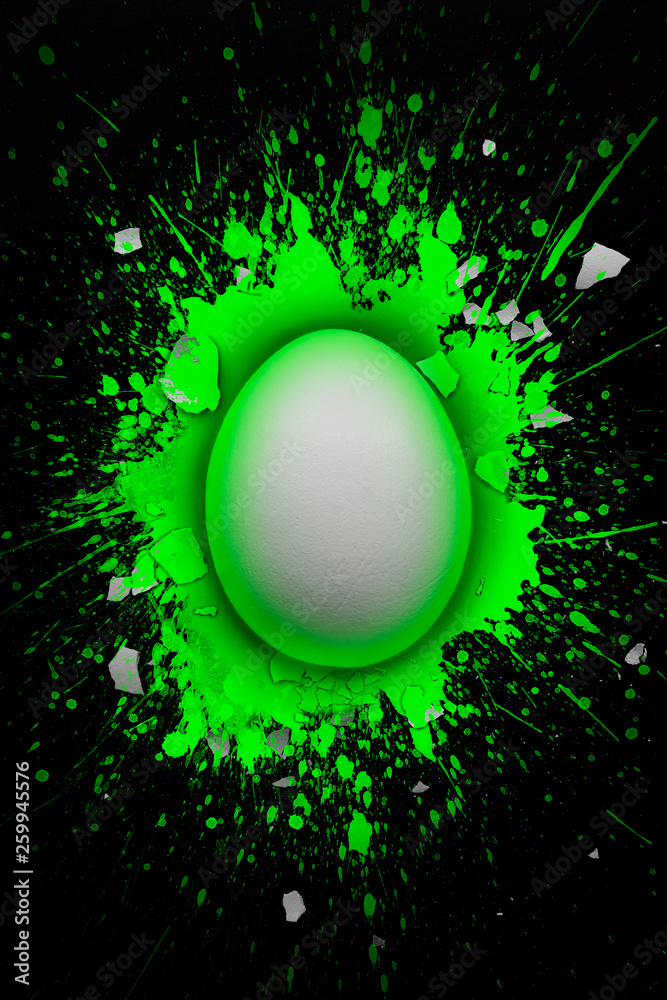Fototapeta premium White egg in a puddle of green color with pieces of broken egg shell around it, Easter concept