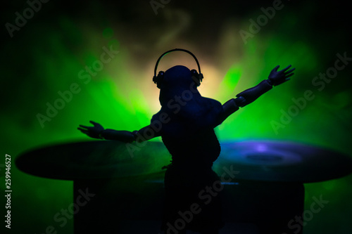 Dj club concept. Woman DJ mixing, and Scratching in a Night Club. Girl silhouette on dj's deck, strobe lights and fog on background. Creative artwork decoration with toy.