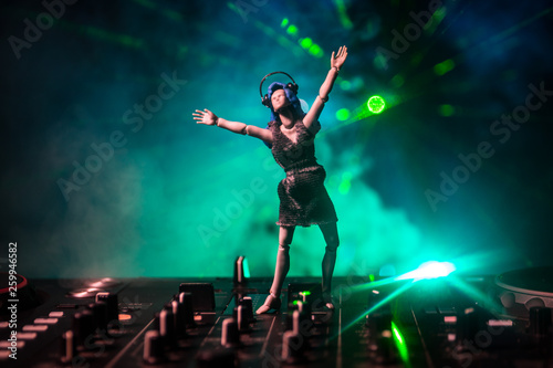 Dj club concept. Woman DJ mixing, and Scratching in a Night Club. Girl silhouette on dj's deck, strobe lights and fog on background. Creative artwork decoration with toy. © zef art