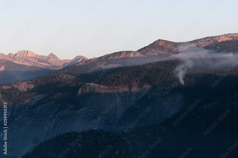 Distant controlled fire burns in the Sierra Nevada Mountains at dusk in Yosemite