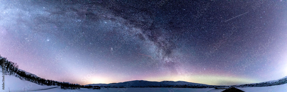 Panoramic view of Milky Way above frozen lake and Scandinavian Mountains in Norway, very cold winter night, deep clear sky