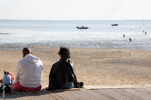 Rear view of couple sitting on a wooden by sea beach