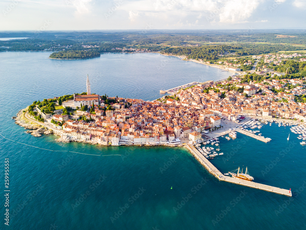 Croatian town of Rovinj on a shore of blue azure turquoise Adriatic Sea, lagoons of Istrian peninsula, Croatia. High bell tower, red tiled roofs of historical buildings, sailboat, piers. Aerial view