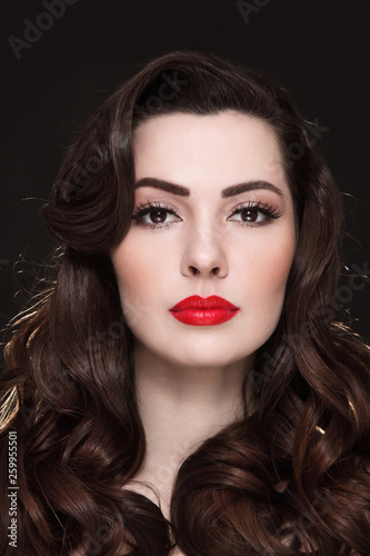 Portrait of young beautiful brunette with curly hair and red lipstick