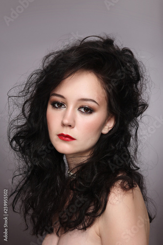 Portrait of young beautiful brunette with messy curly hair and red lipstick