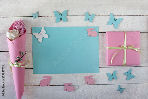 Wiosenne tło z niebieską kartą, prezentem przewiązanym wstążką, kwiatami, motylami i zajączkami