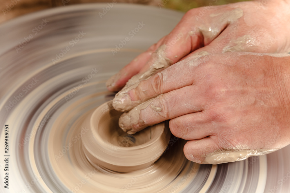 Rotating potter's wheel and clay ware on it taken from above. A sculpts his hands with a clay cup on a potter's wheel. Hands in clay.