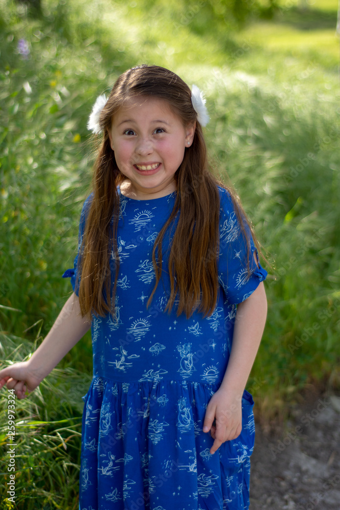 Little Girl in Blue Dress making funny and crazy face with tongue out in front of green field Little Girl in Blue Dress making funny and crazy face with tongue out in front of green field