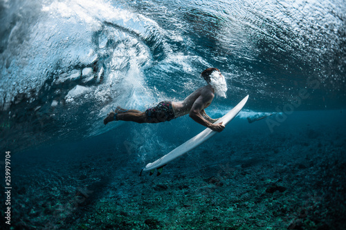Surfer performs dive (the duck dive) with his surfboard under the wave and exhales air into the water.