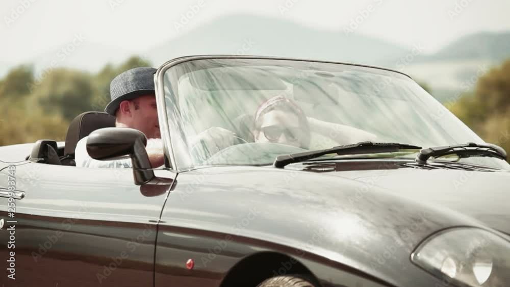 Couple cheerfully talking in convertible car, then setting off Couple cheerfully talking in convertible car, then setting off