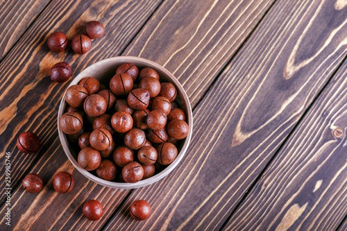 Macadamia nuts in a wooden bowl on a wooden background with copy space.