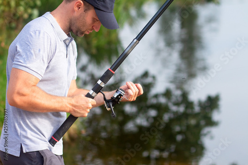 Fisherman preparing bait on fishing rod on lakeside in morning