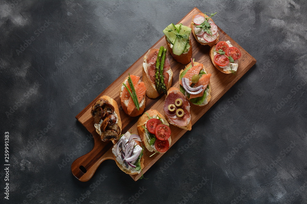 Brushetta or traditional Spanish-tapas. Appetizers with Italian antipasti snacks. Variety of small sandwiches with prosciutto,cherry tomatoes, salmon, cream cheese, cucumber, radish, asparagus