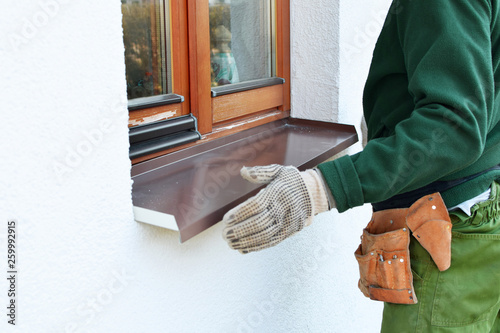 Man worker in protective gloves installing sill on external wooden window frame on white house facade. Sill installation process. Exterior design, building, home improvement, diy concept.